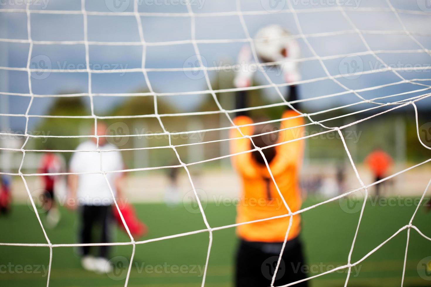 Un juego de fútbol con la red en foco mientras un portero detiene la pelota foto