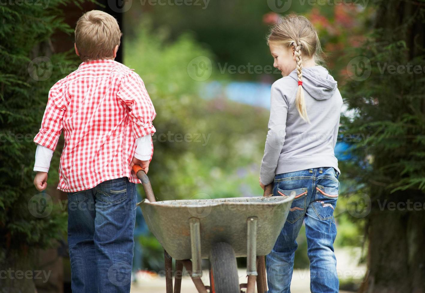 Dos niños jugando con carretilla en jardín foto