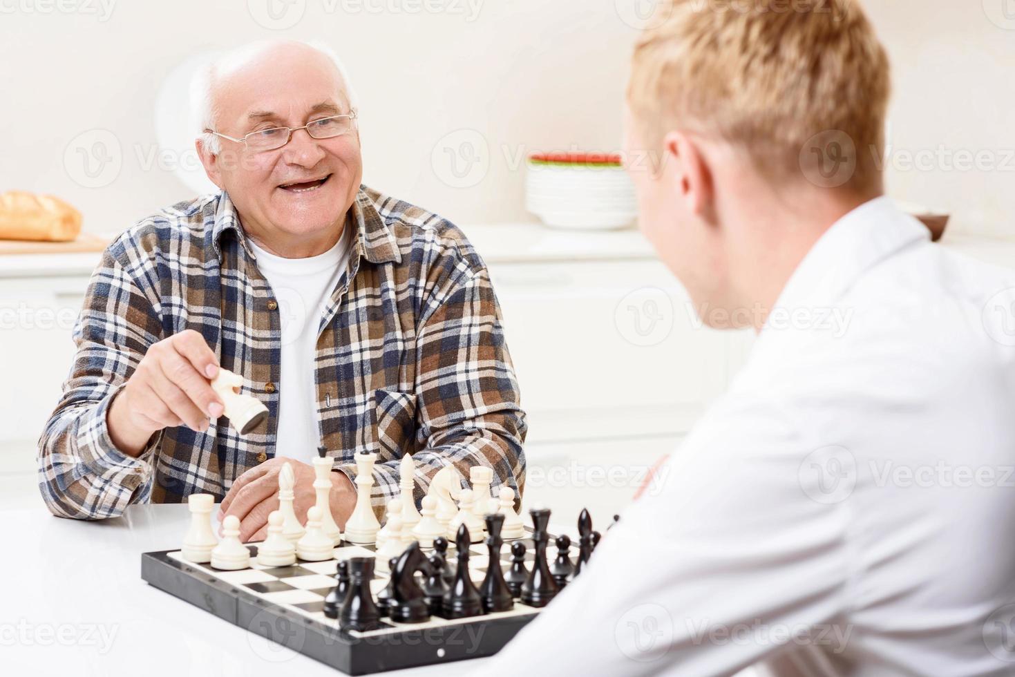 Grandson and grandfather playing chess in kitchen photo