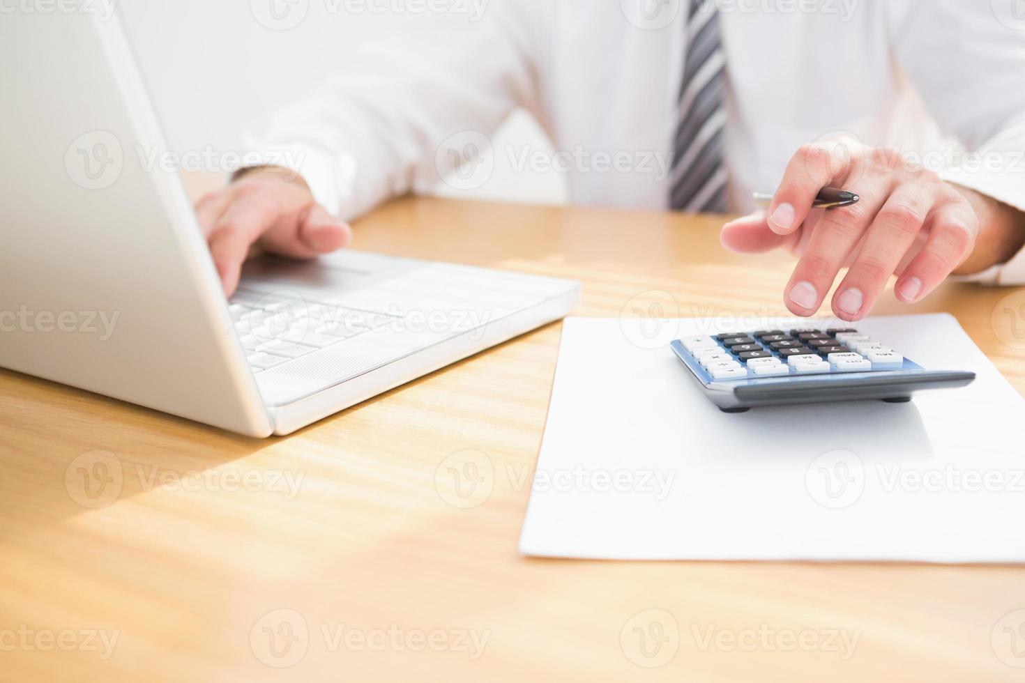 Un empresario en su escritorio usando una computadora y una calculadora foto