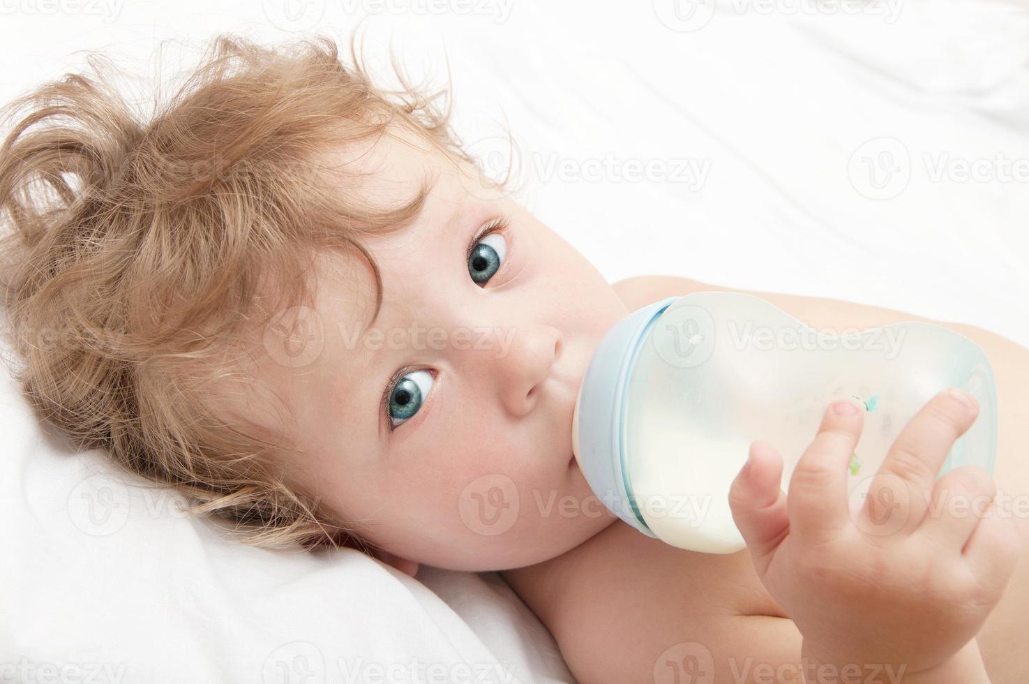 pequeño bebé de cabeza rizada chupa una botella de leche foto