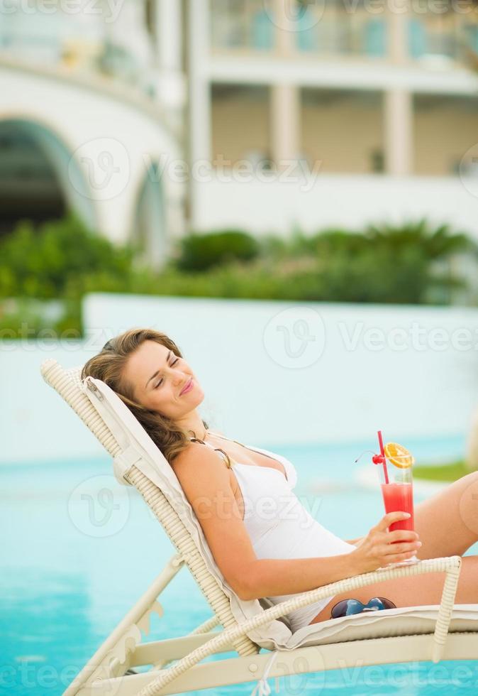 Happy young woman with cocktail enjoying laying on chaise-longue photo