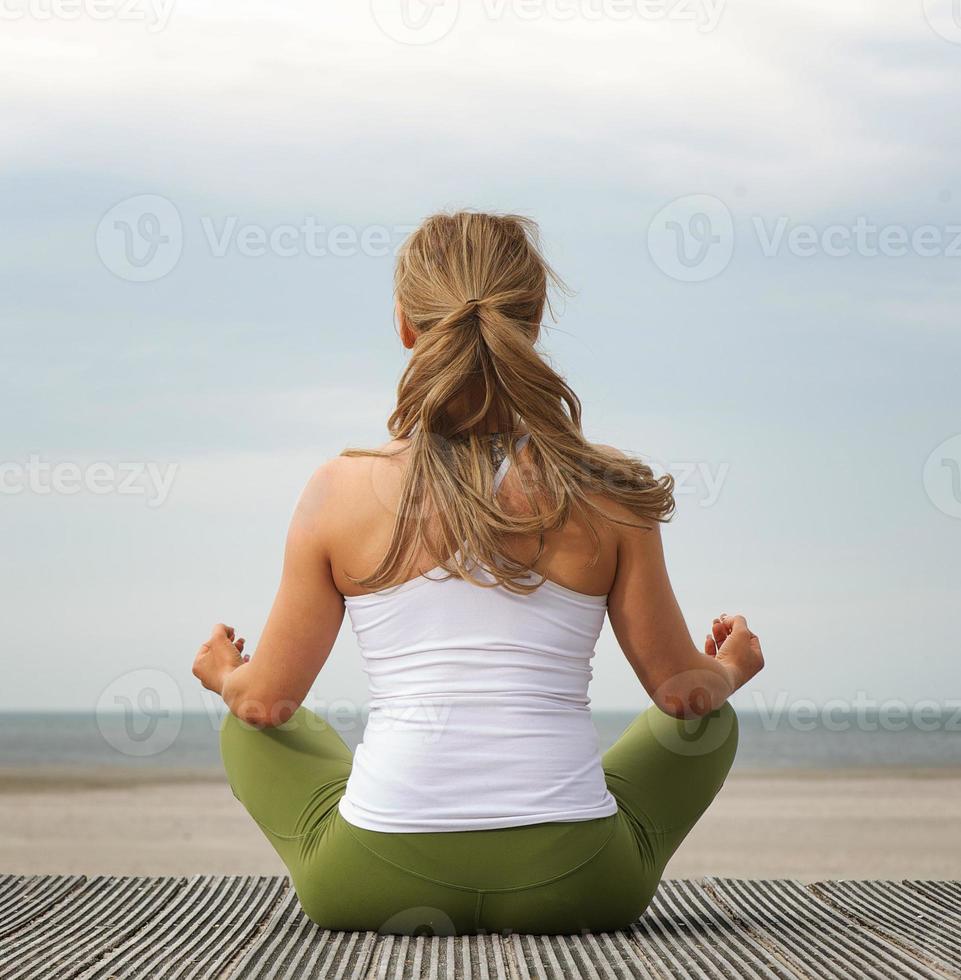 Rear view young woman in yoga pose at the beach photo