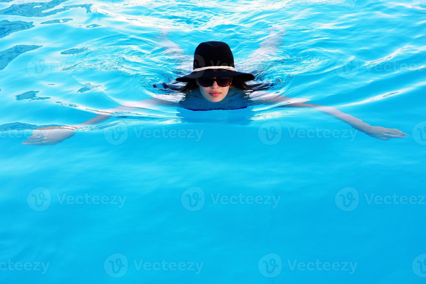 mujer con gafas de sol y sombrero nadando en la piscina foto