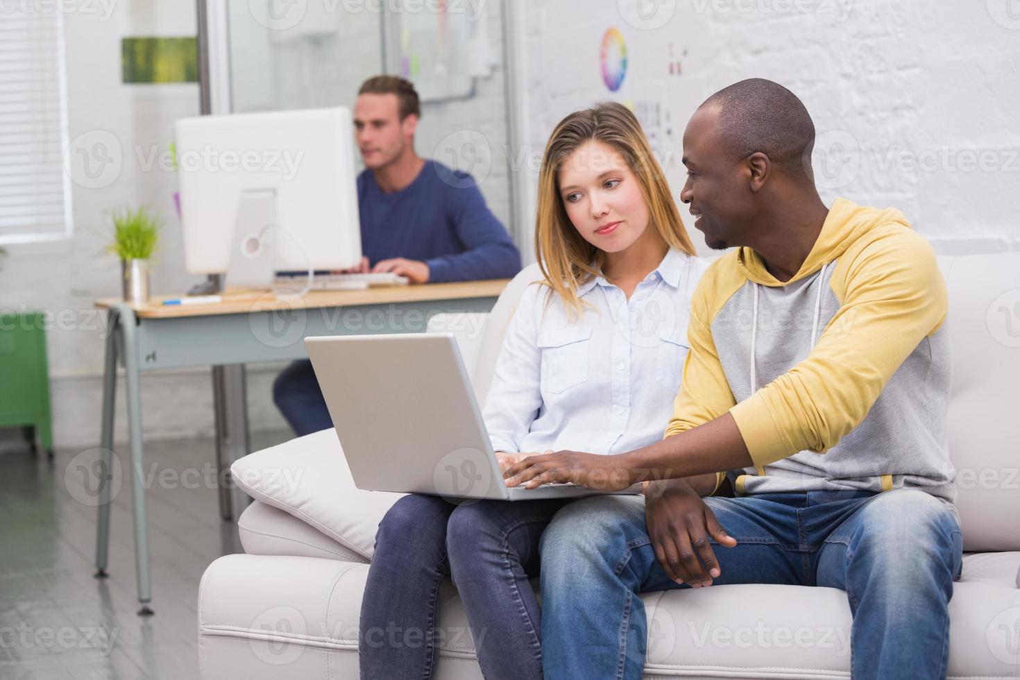 Casual colleagues using laptop on couch in office photo