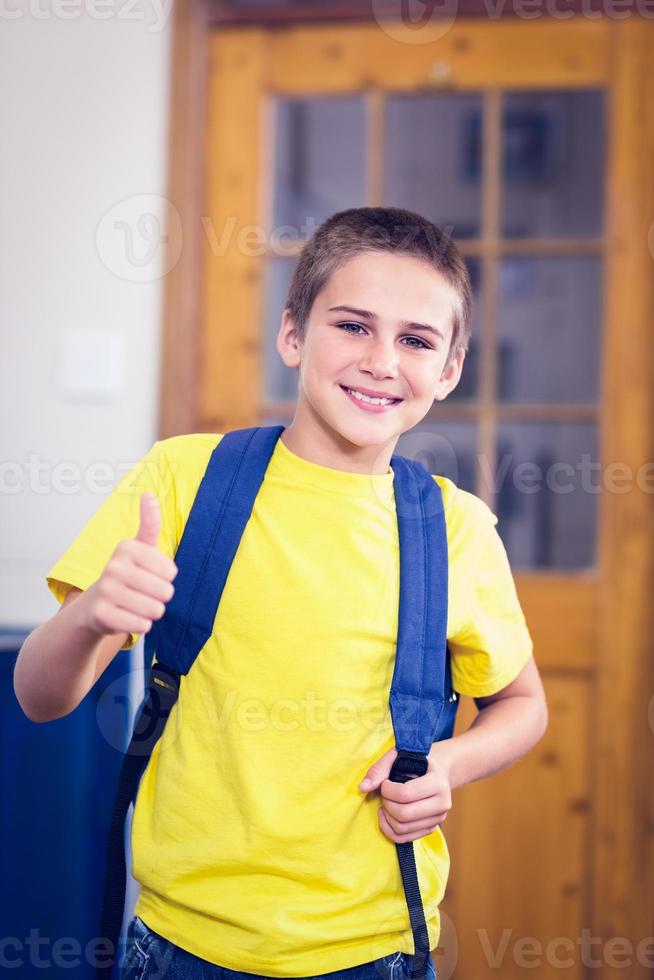 alumno sonriente con mochila haciendo pulgares en un aula foto