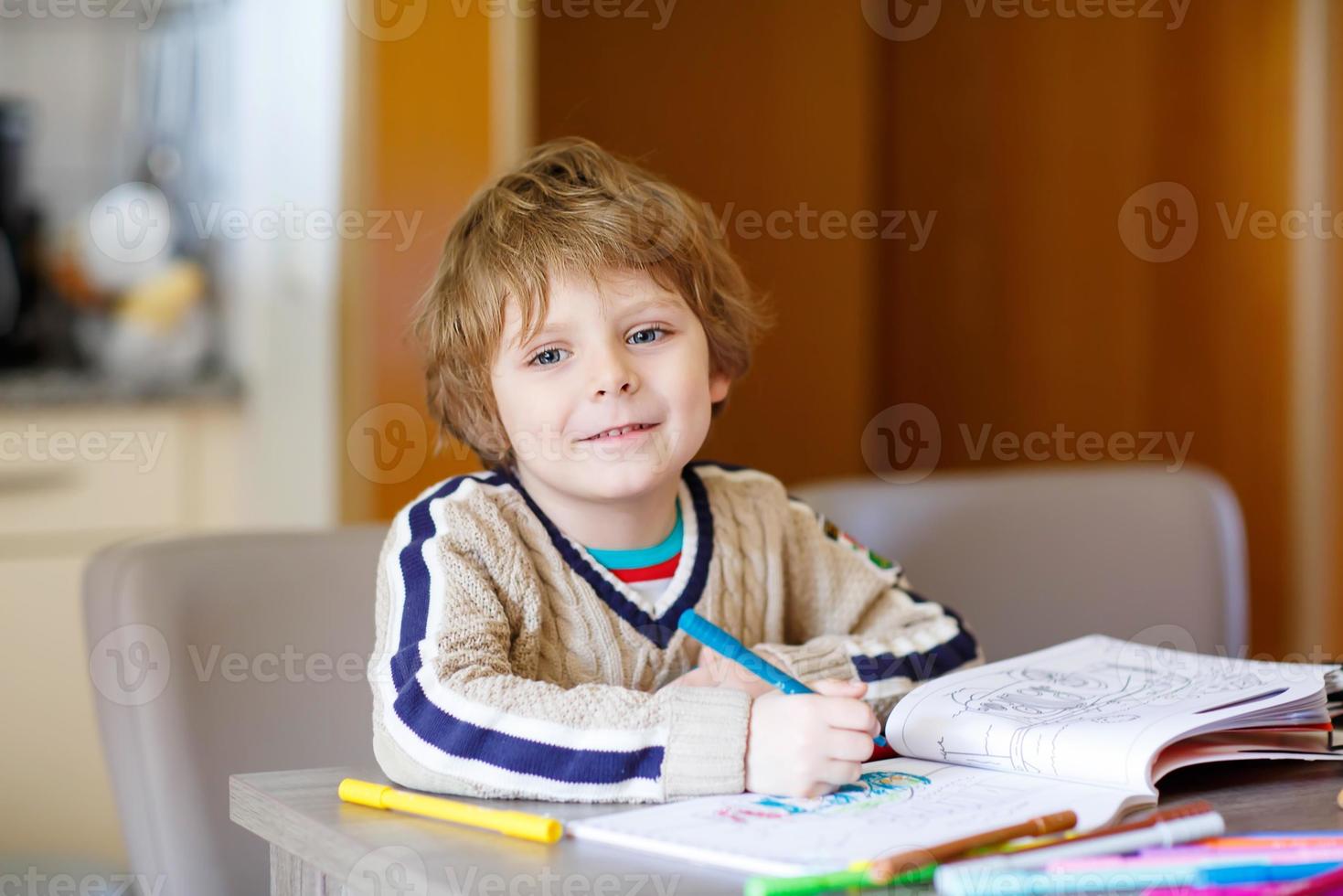 Cute happy schoolkid at home making homework photo