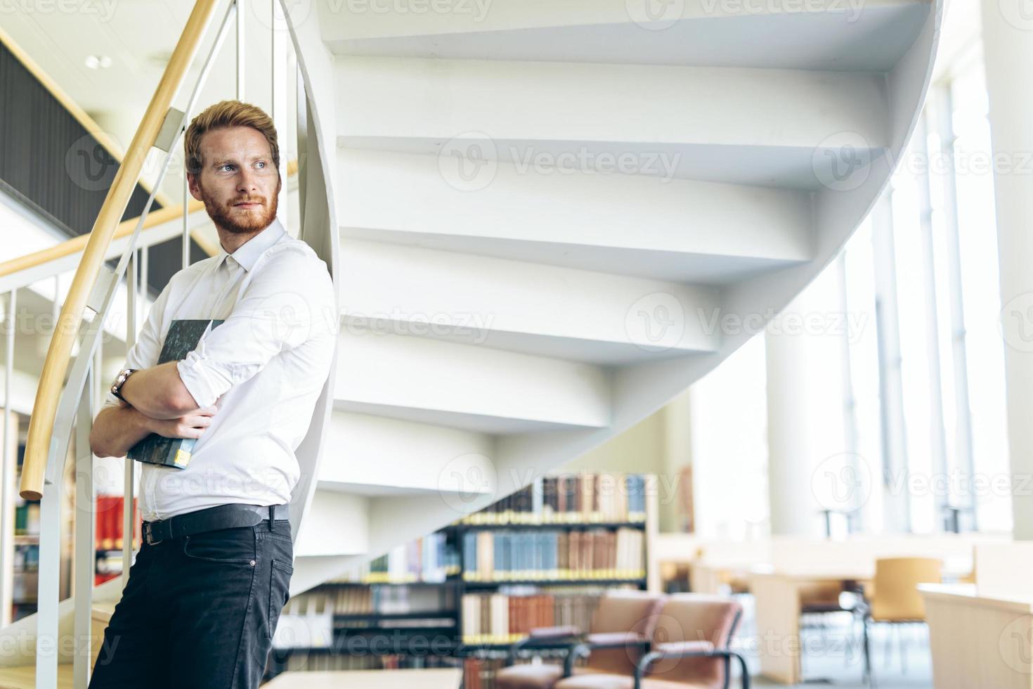 Handsome intelligent guy reading a book in a library photo