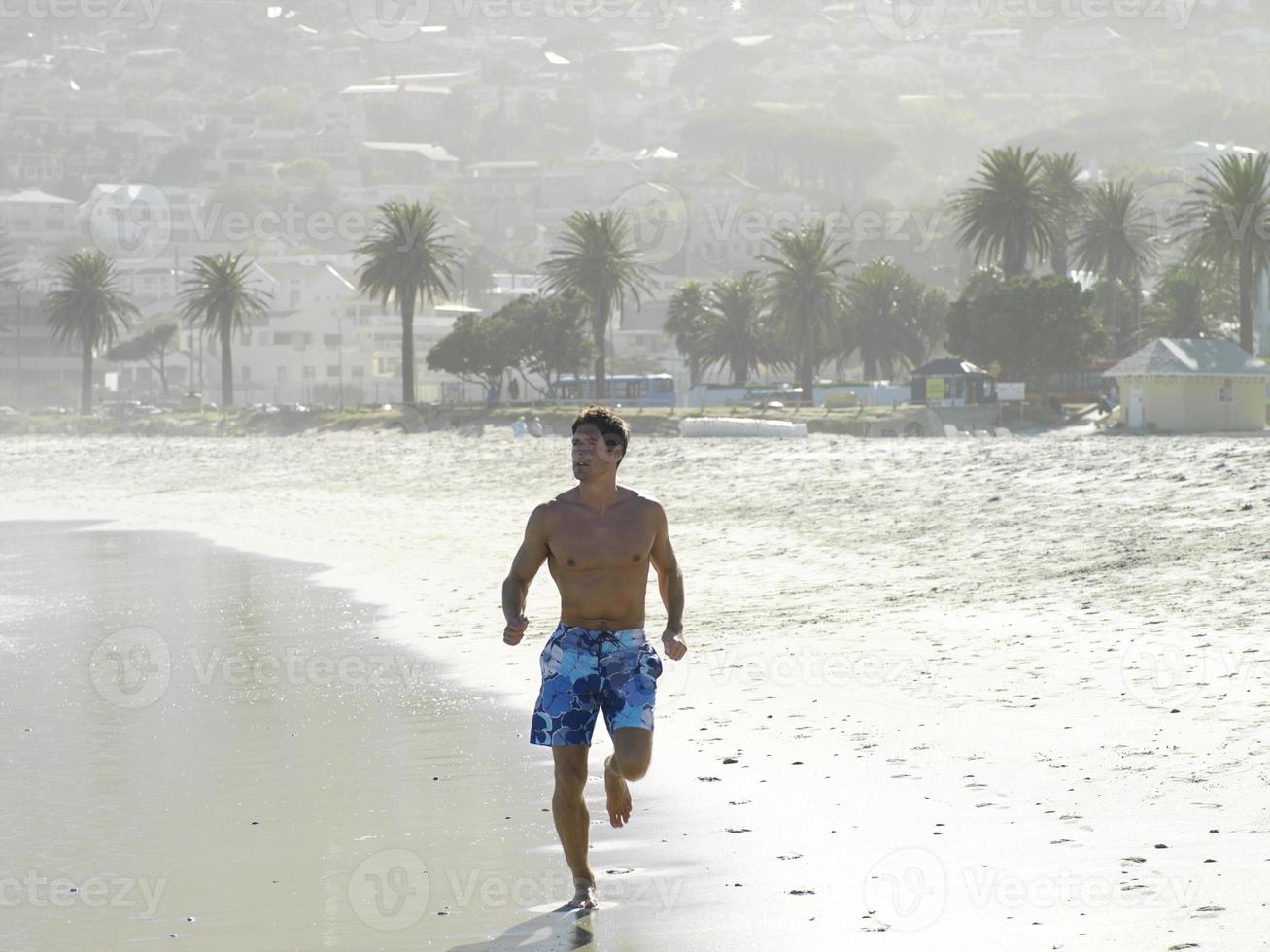 hombre en shorts de baño para correr a lo largo de la playa de arena foto
