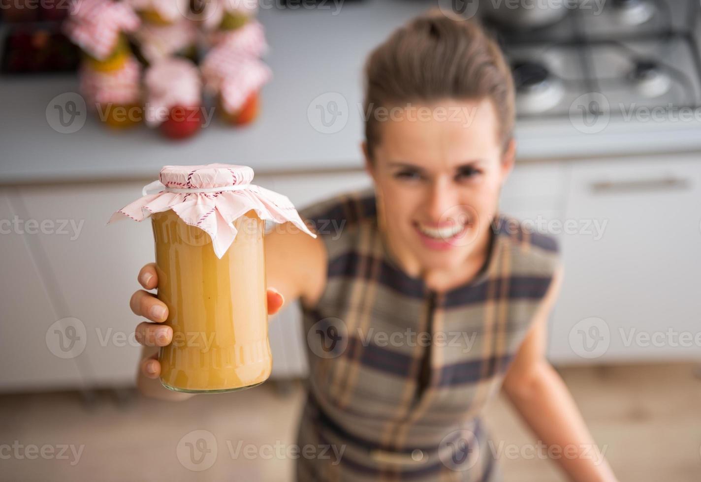 Closeup on happy housewife showing jar with homemade apple jam photo
