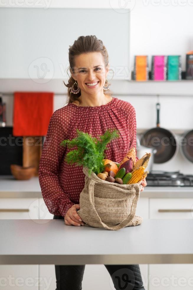 Happy young housewife with local market purchases in kitchen photo