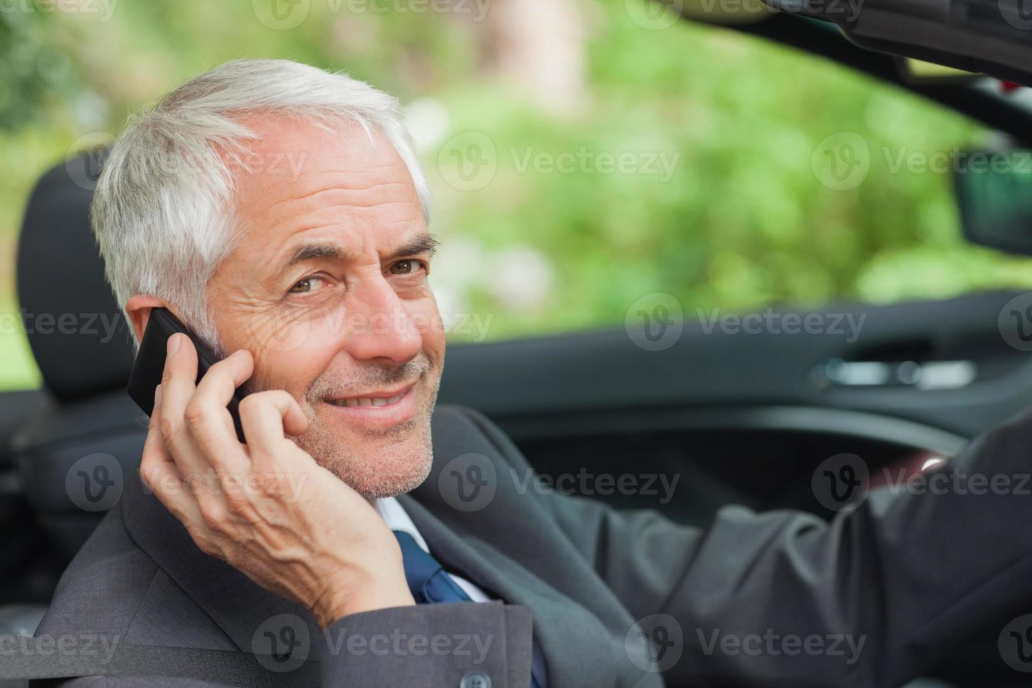 empresario alegre en el teléfono conduciendo cabriolet caro foto