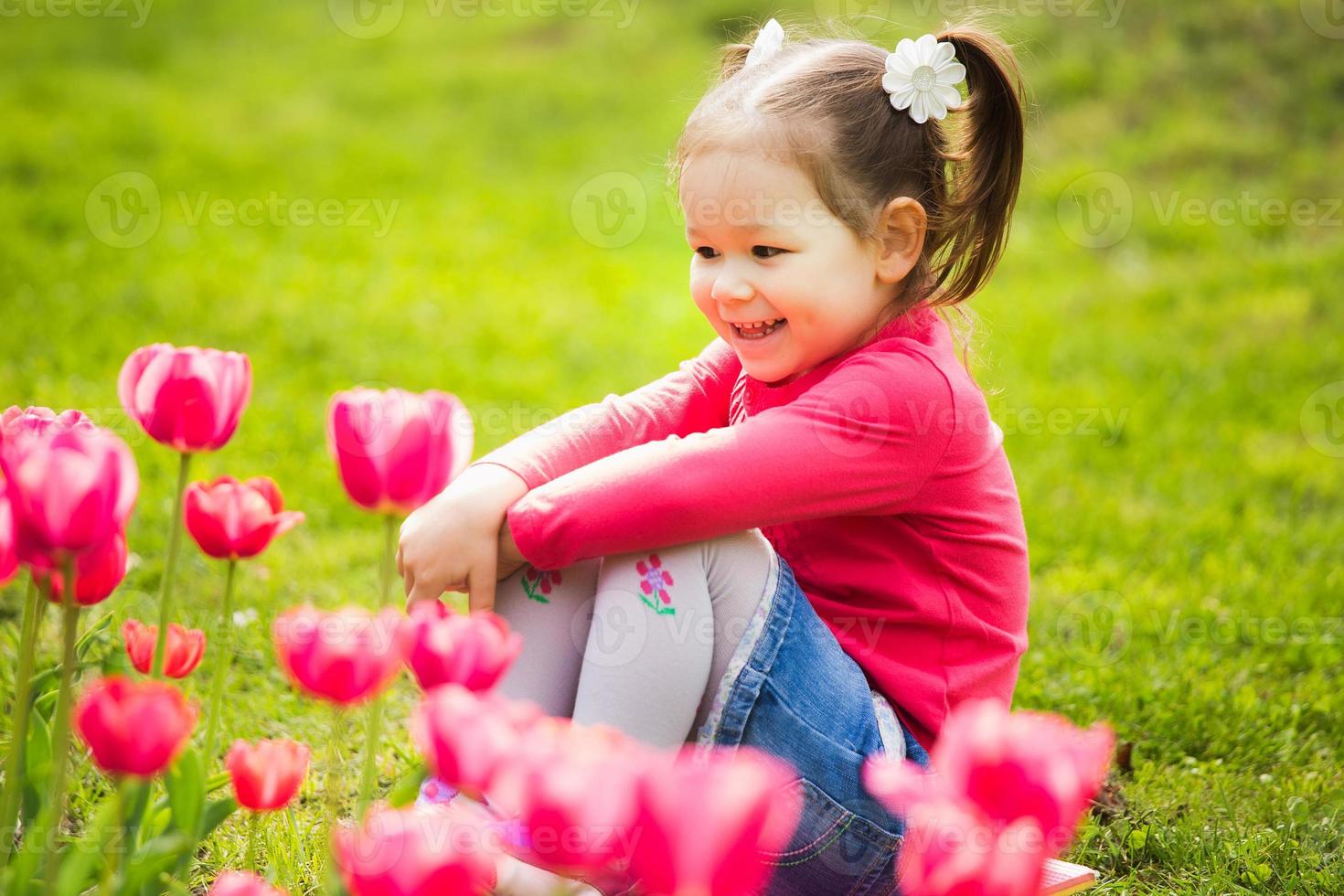 alegre niña sentada en la hierba mirando tulipanes foto