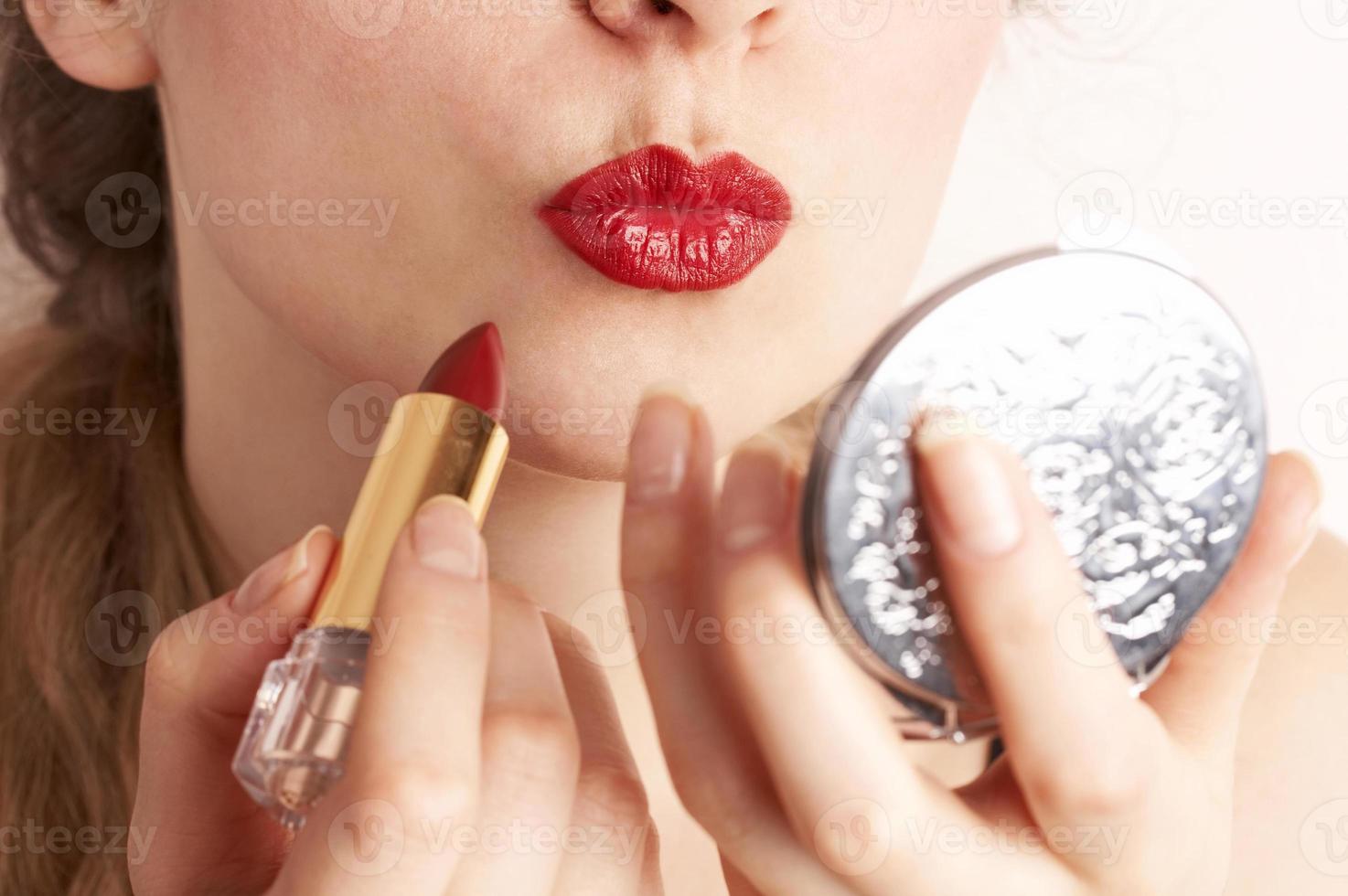 Woman applying red lipstick while looking to hand mirror photo