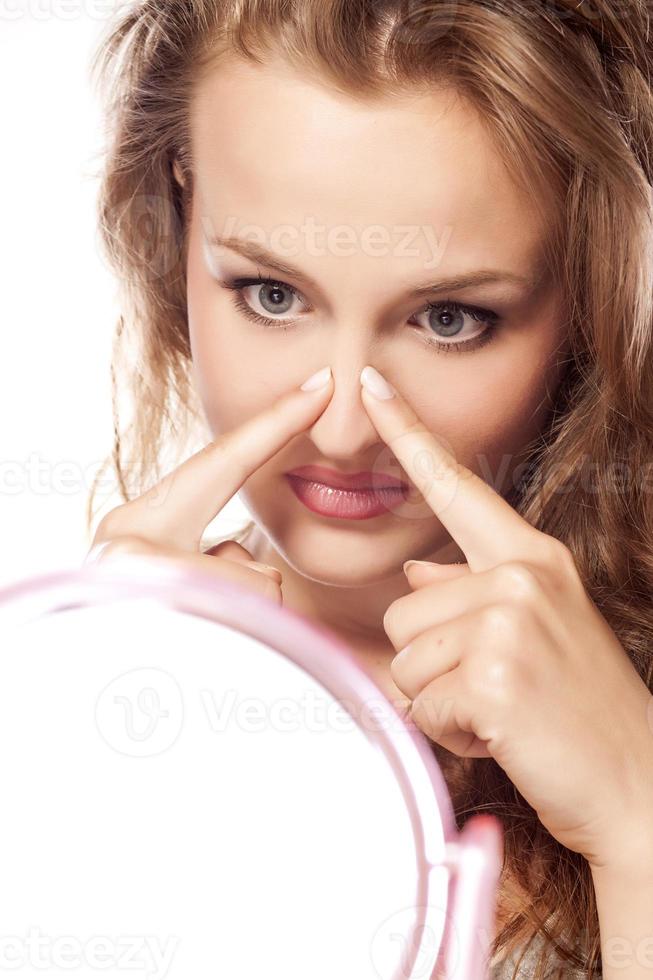Disappointed young blonde touching her nose in the mirror photo