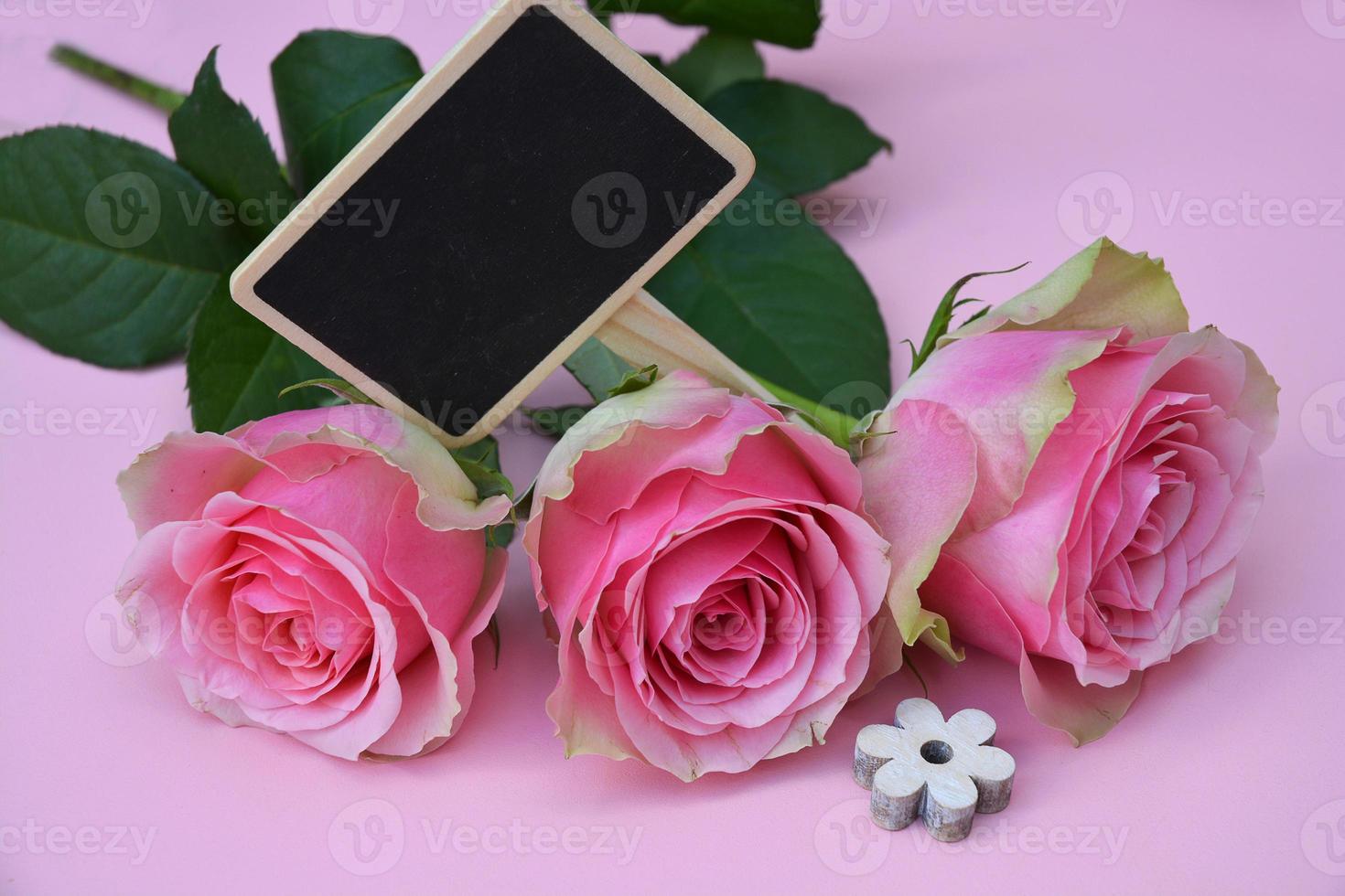 Fondo rosa y rosas, con etiqueta de pizarra negra vacía foto