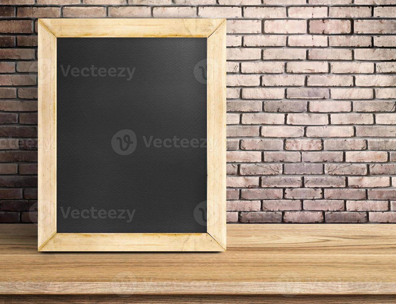 Blank blackboard on wooden table at red brick wall photo