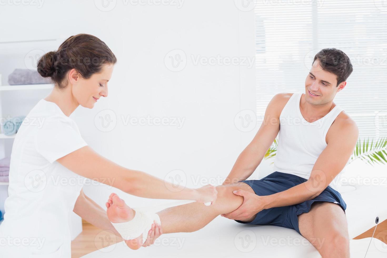 Doctor bandaging her patient ankle photo