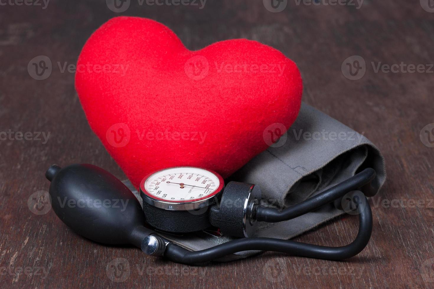 médico, medir la presión arterial con corazón rojo en la mesa de madera foto