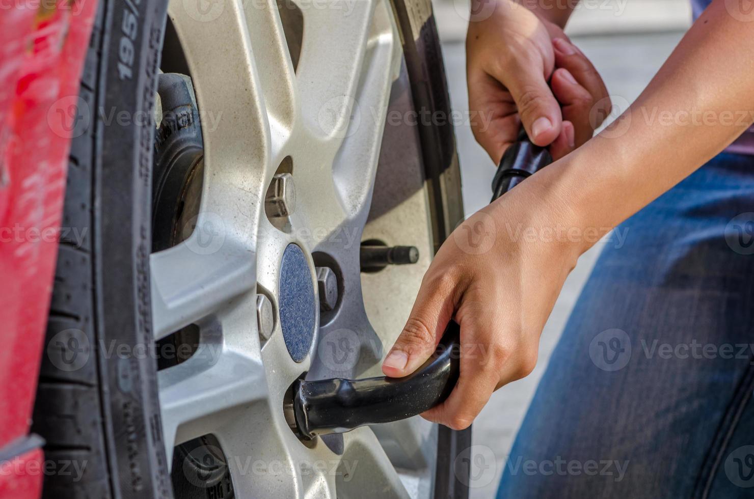 La mujer está cambiando el neumático con una llave de rueda foto