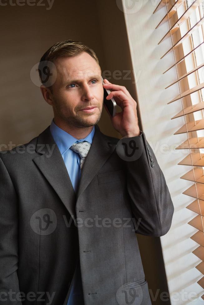 Businessman peeking through blinds while on call photo