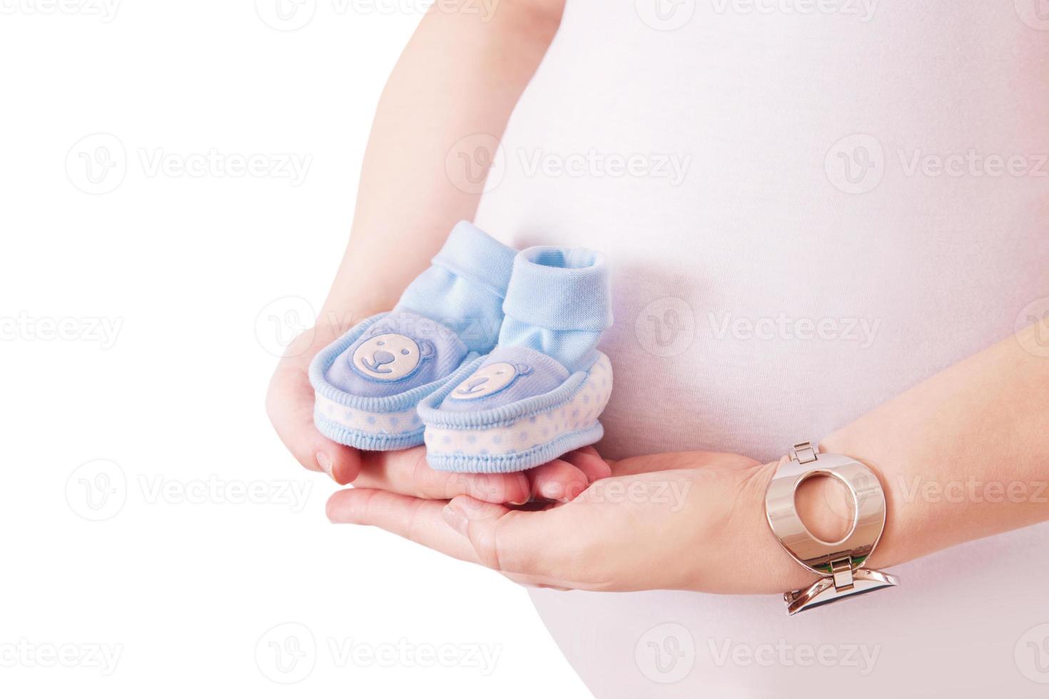 Pregnant woman holding pair of blue shoes for baby photo