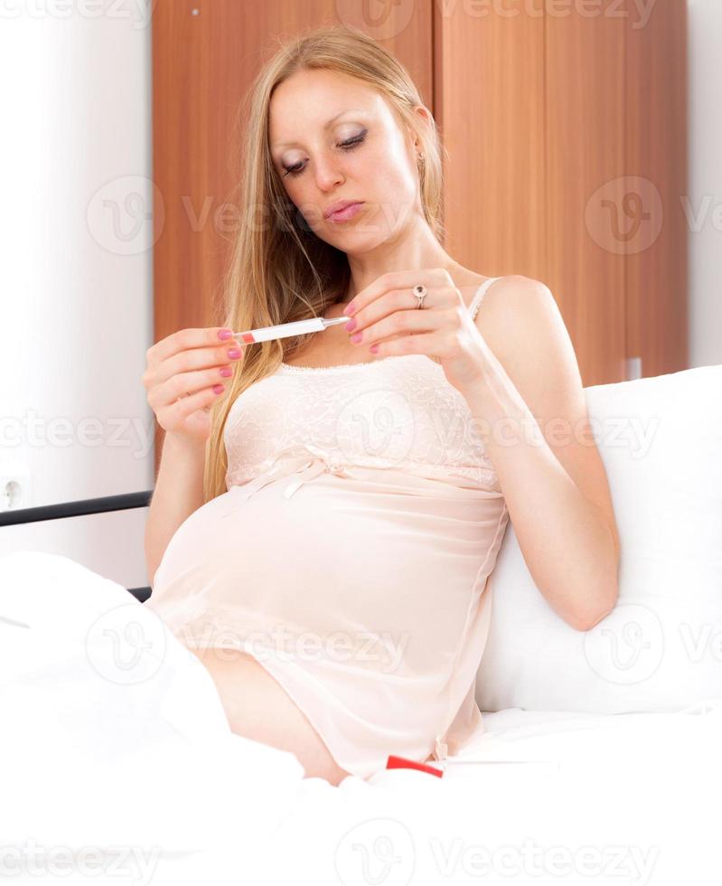 Pregnant woman measures the temperature with thermometer in  bed photo