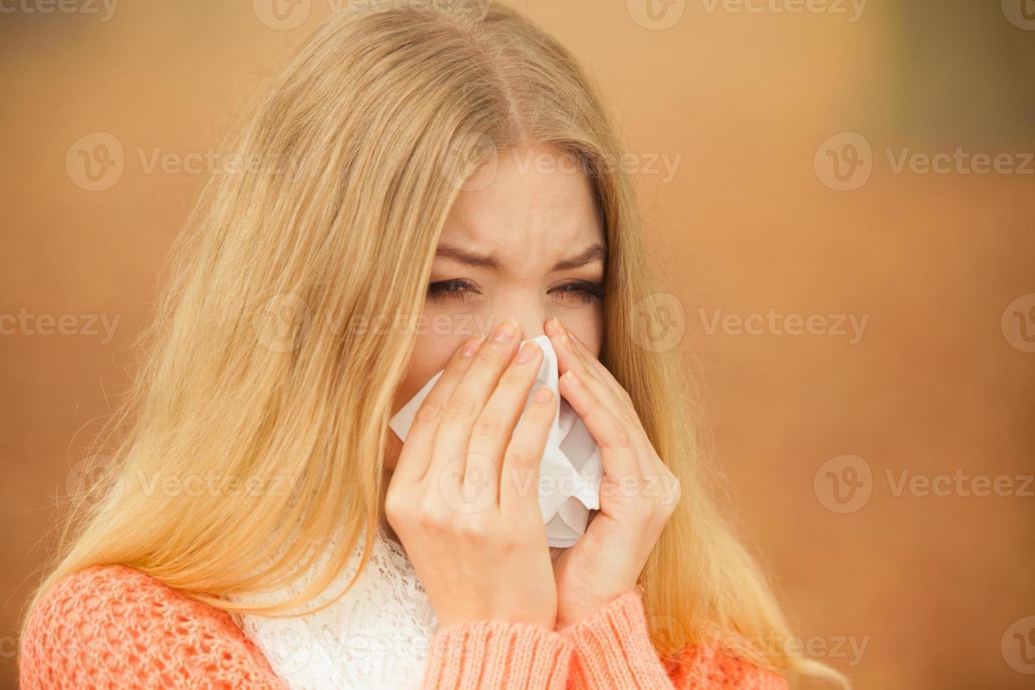 Sick ill woman in autumn park sneezing in tissue. photo
