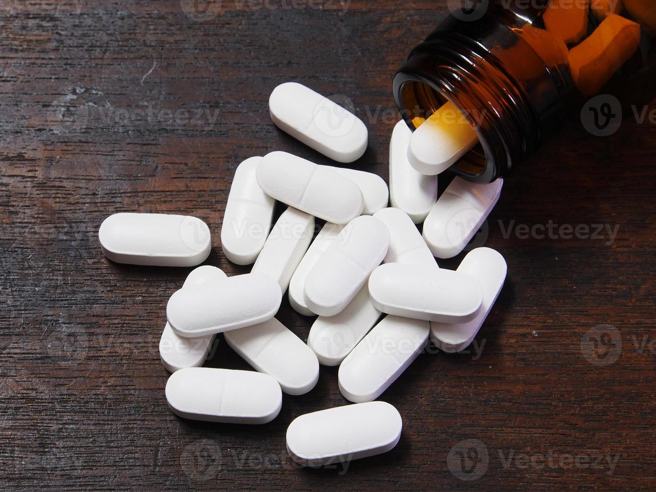 Pills spilling out of a pill bottle on wooden table photo