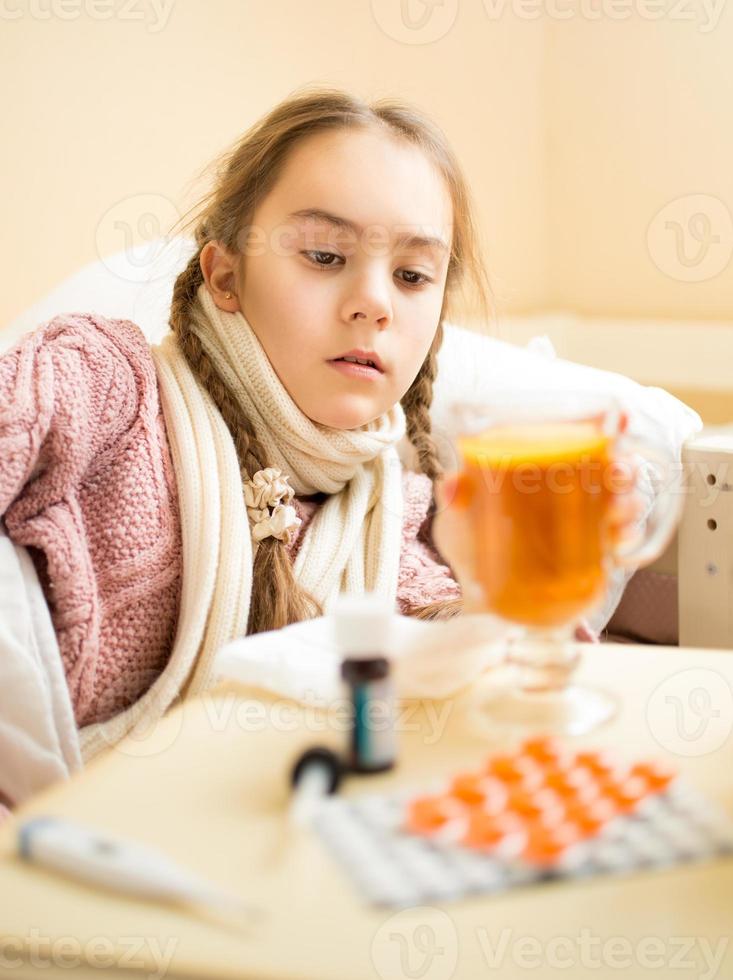 Chica con gripe acostada y mirando la taza de té foto