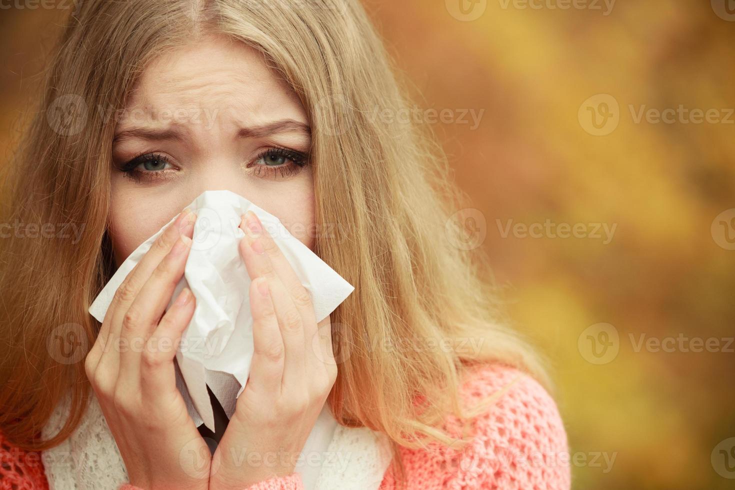 Sick ill woman in autumn park sneezing in tissue. photo