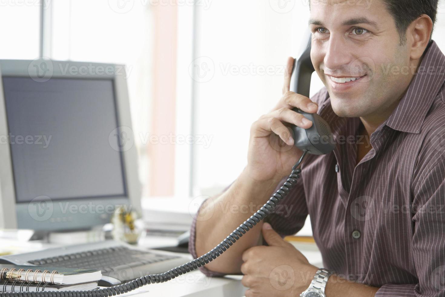 Happy Businessman Using Landline Phone In Office photo