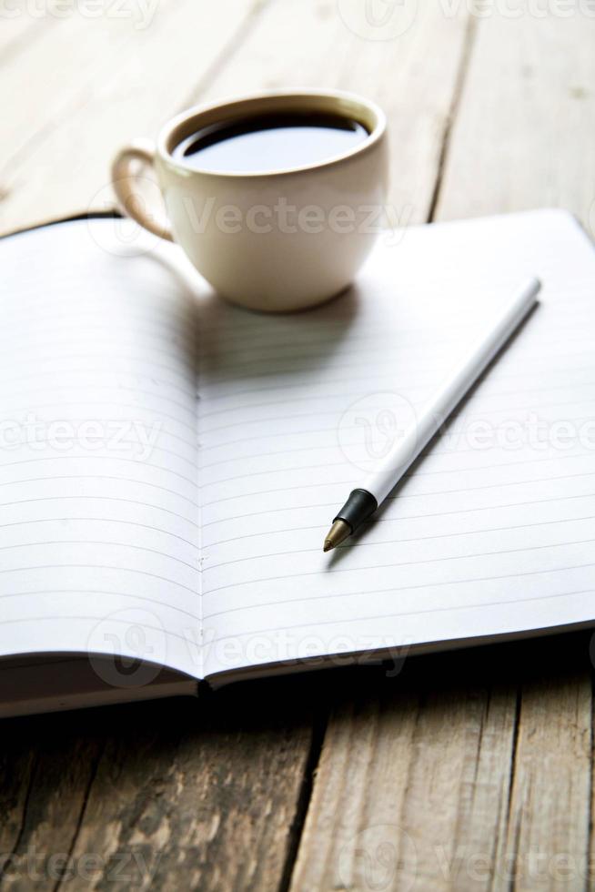 cuaderno con bolígrafo y café en la mesa de madera vieja foto