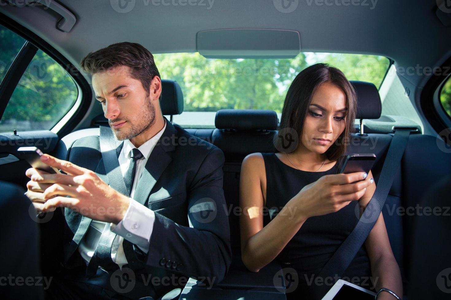 empresario y empresaria con smartphone en coche foto