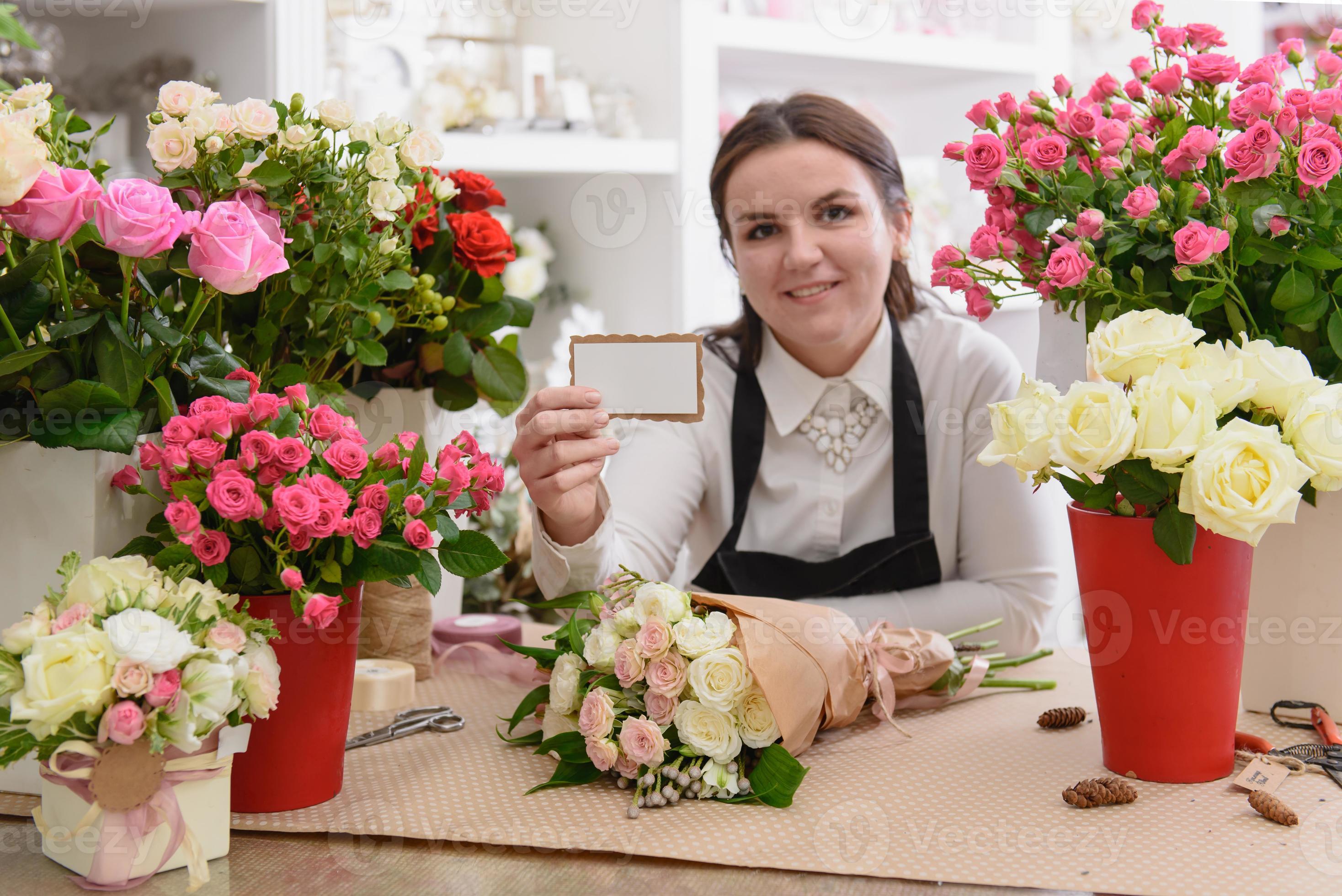Floreria femenina mostrando tarjeta de presentación entre ramos de flores en la tienda foto