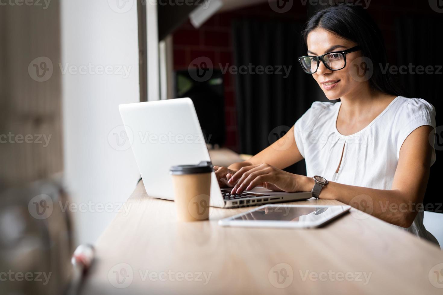 buscando una nueva solución. Pensativo hermosa joven empresaria en gafas trabajando en la computadora portátil mientras está sentado en su lugar de trabajo foto