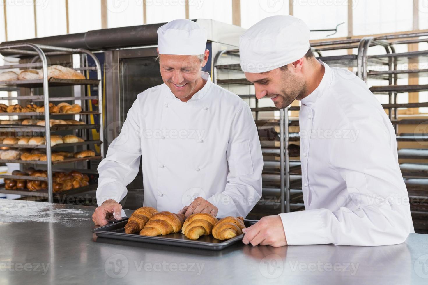 Smiling bakers looking trays of croissants photo