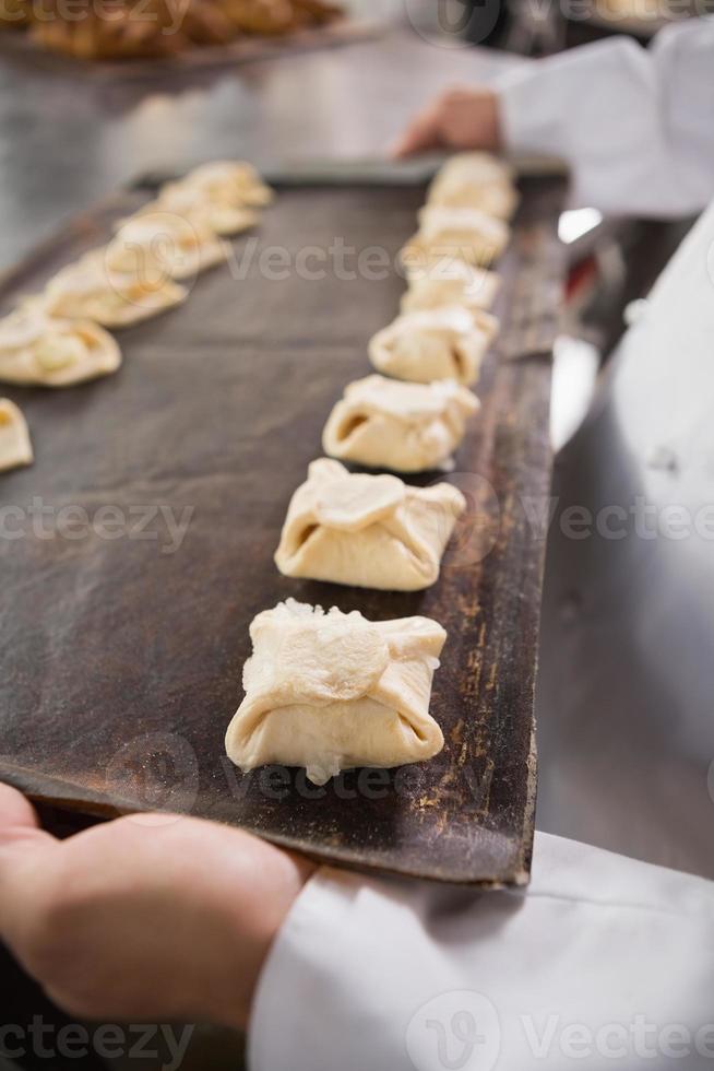 Close up baker holding tray of raw dough photo