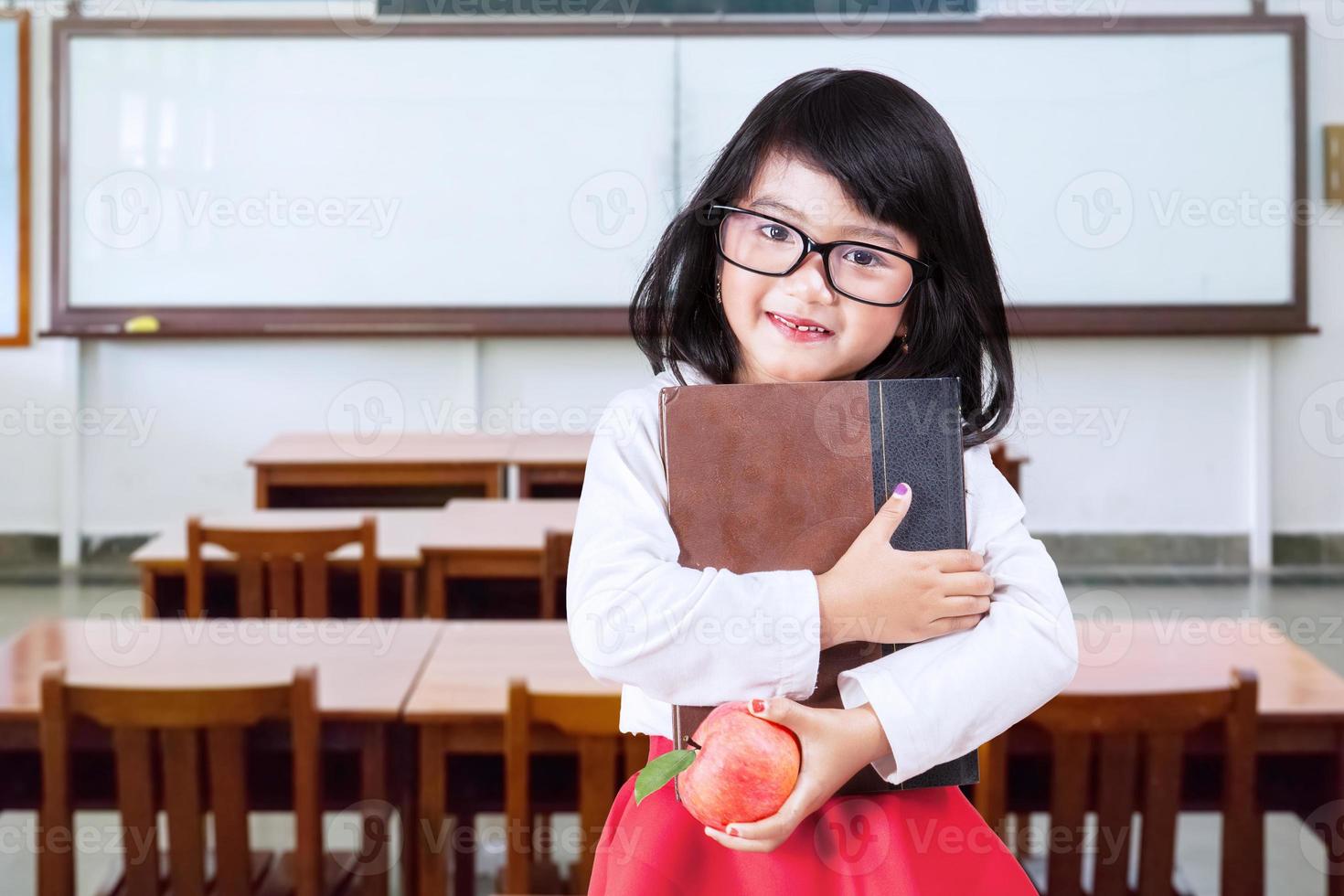 pequeño alumno tiene libro y manzana en clase foto