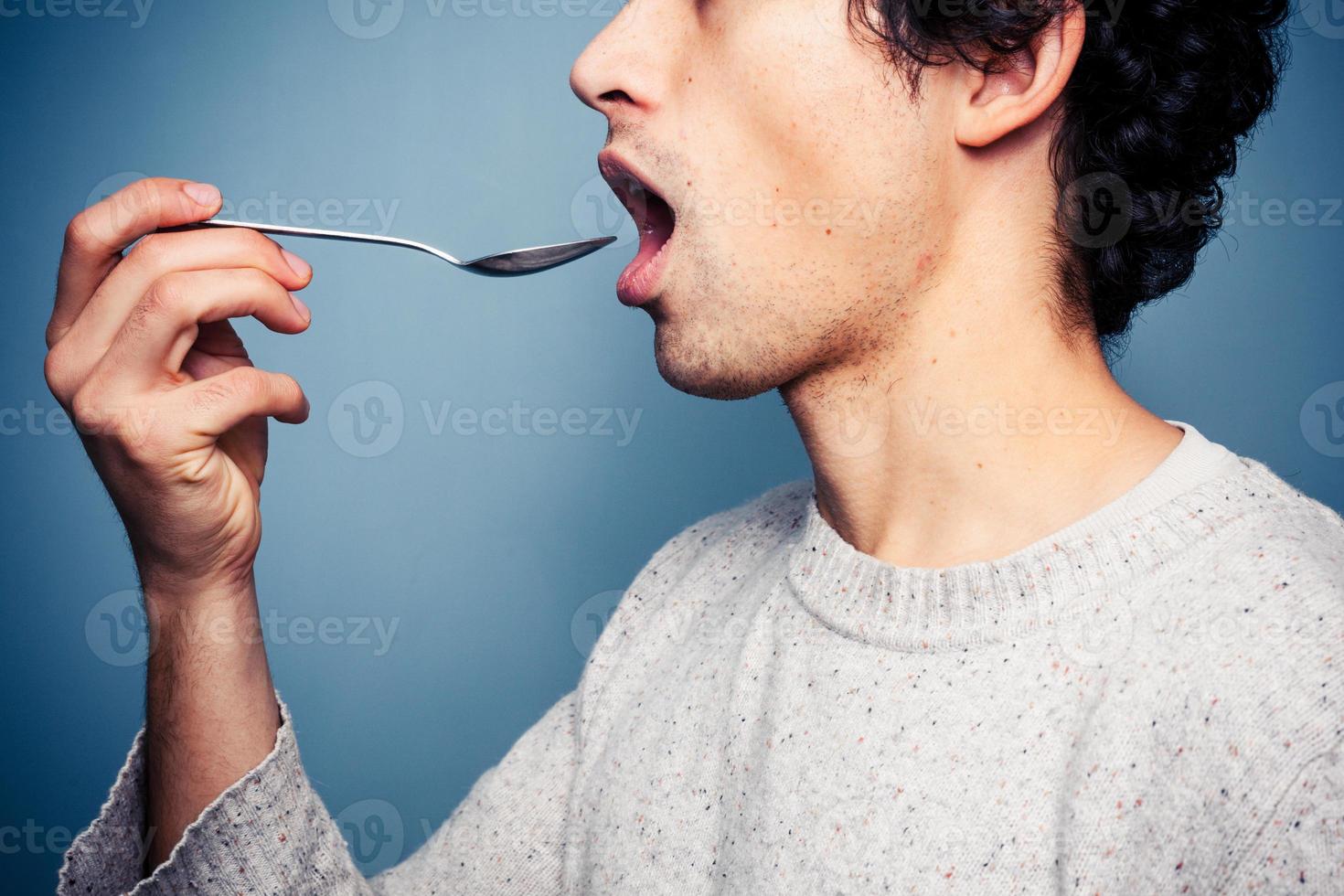 Young man eating from a spoon photo
