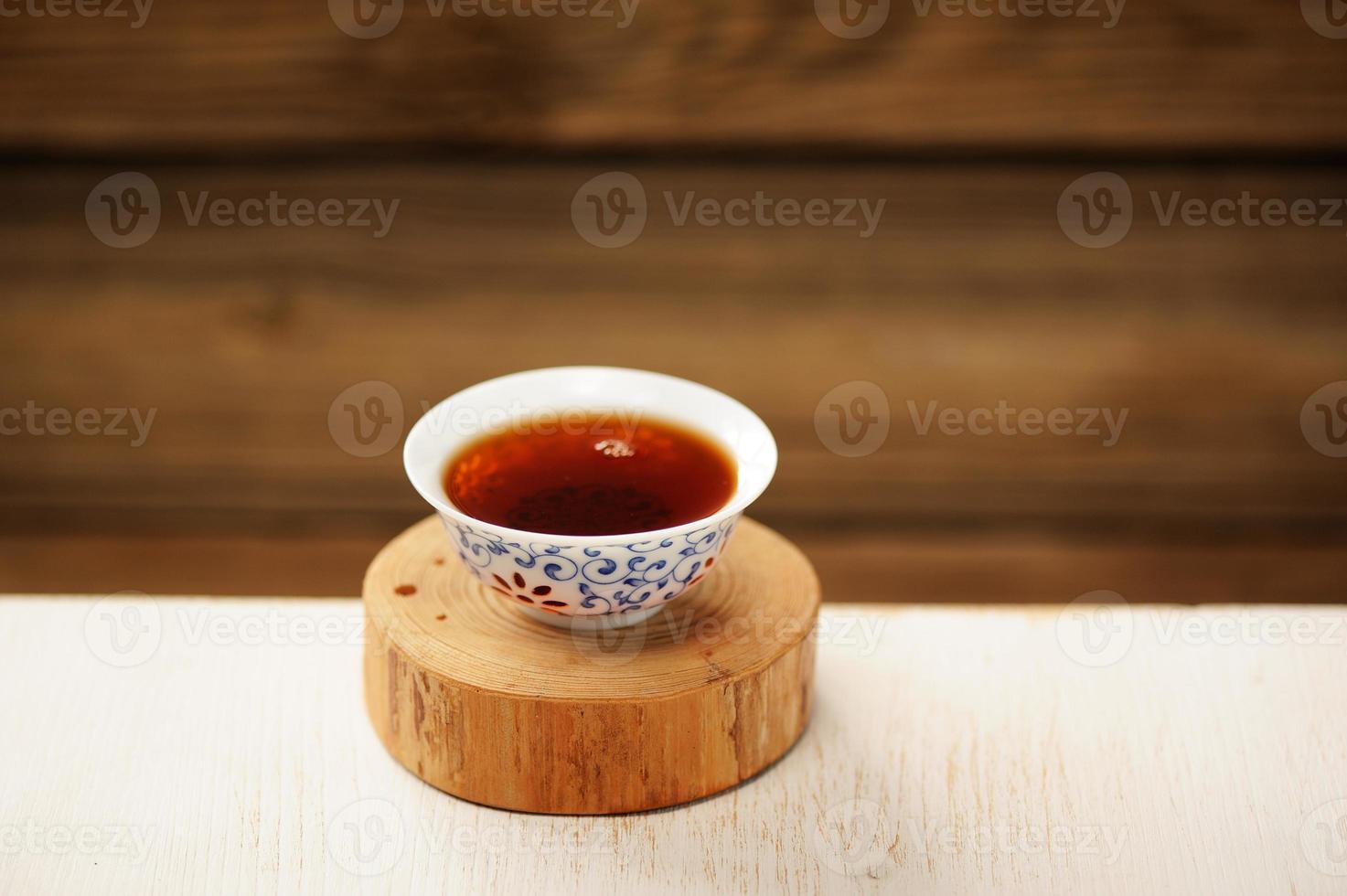 Black puerh tea in white bowl on wooden stand photo