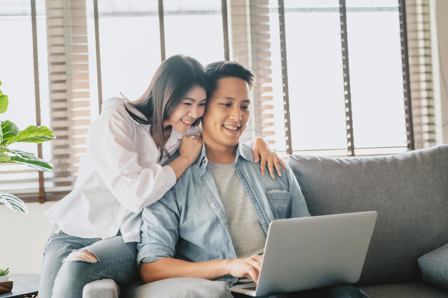 Pareja asiática utilizando la computadora portátil en el sofá en casa foto