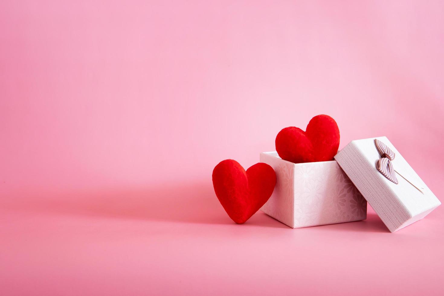 Two red hearts in a gift box on pink background photo