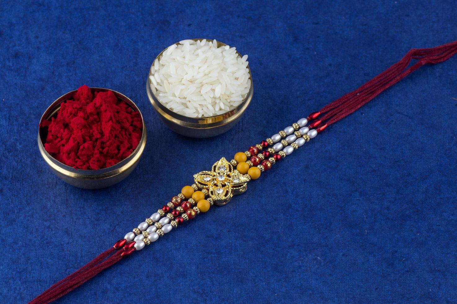 Pulsera rakhi, granos de arroz y kumkum sobre fondo azul. foto