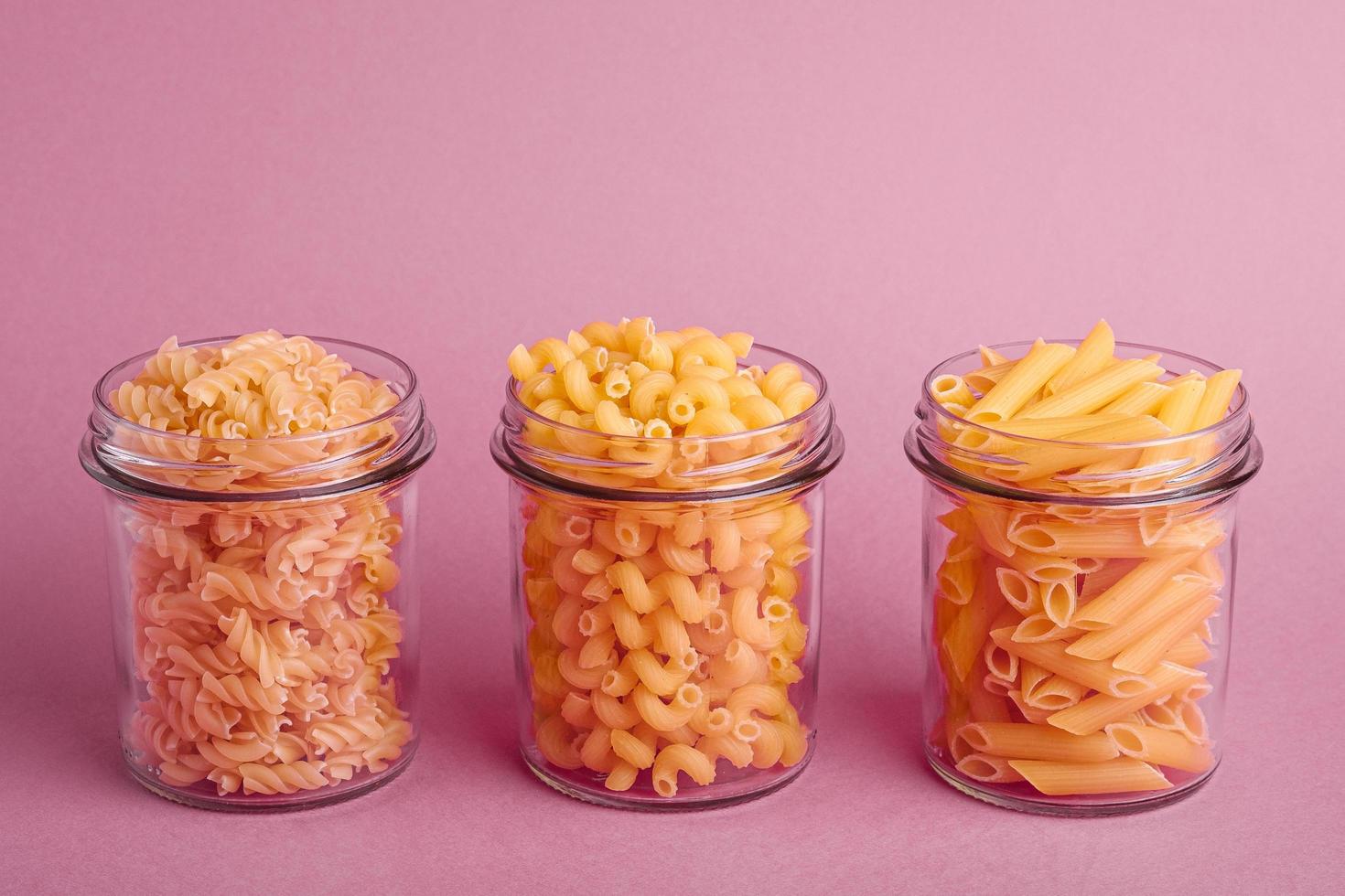 Variety of uncooked golden wheat pasta on minimal pink background photo