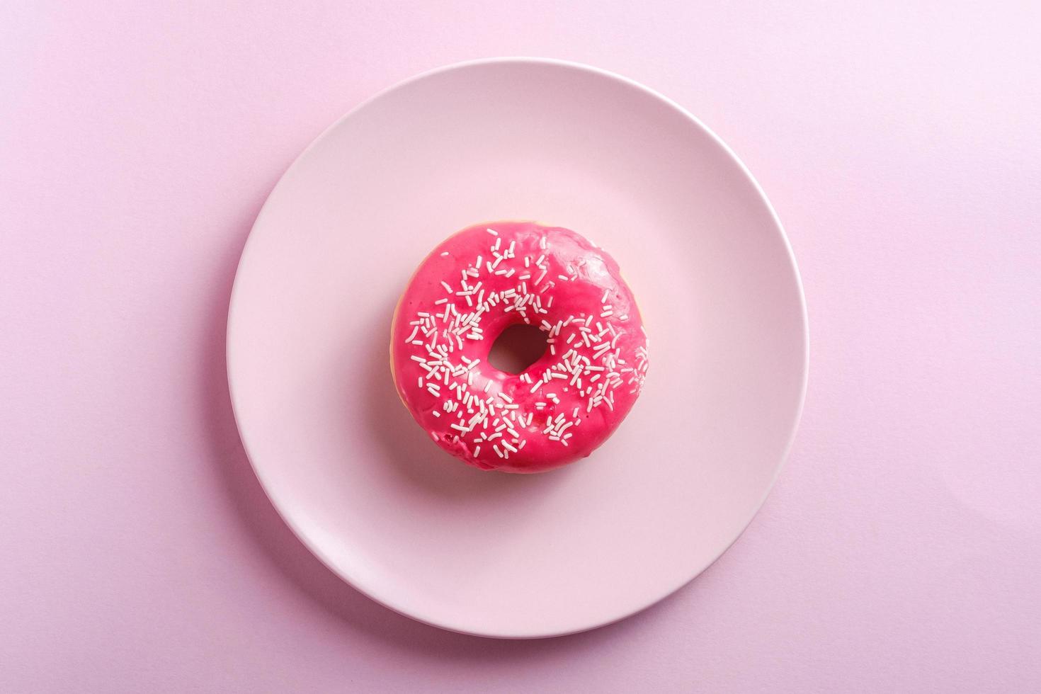 Donut rosa brillante con chispitas blancas en placa rosa foto