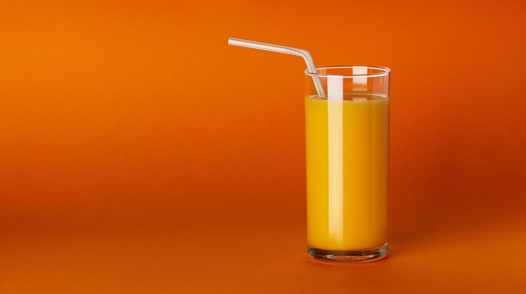 Un vaso de jugo de naranja sobre fondo naranja con espacio de copia foto