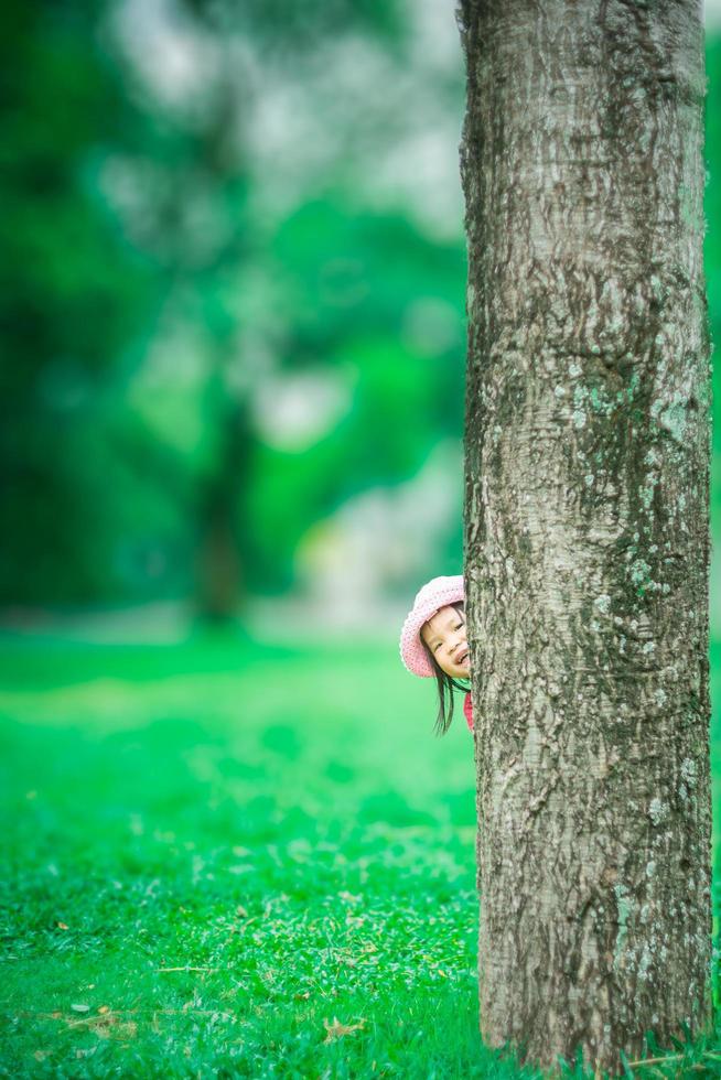 Niña asiática a escondidas detrás del árbol en el bosque foto