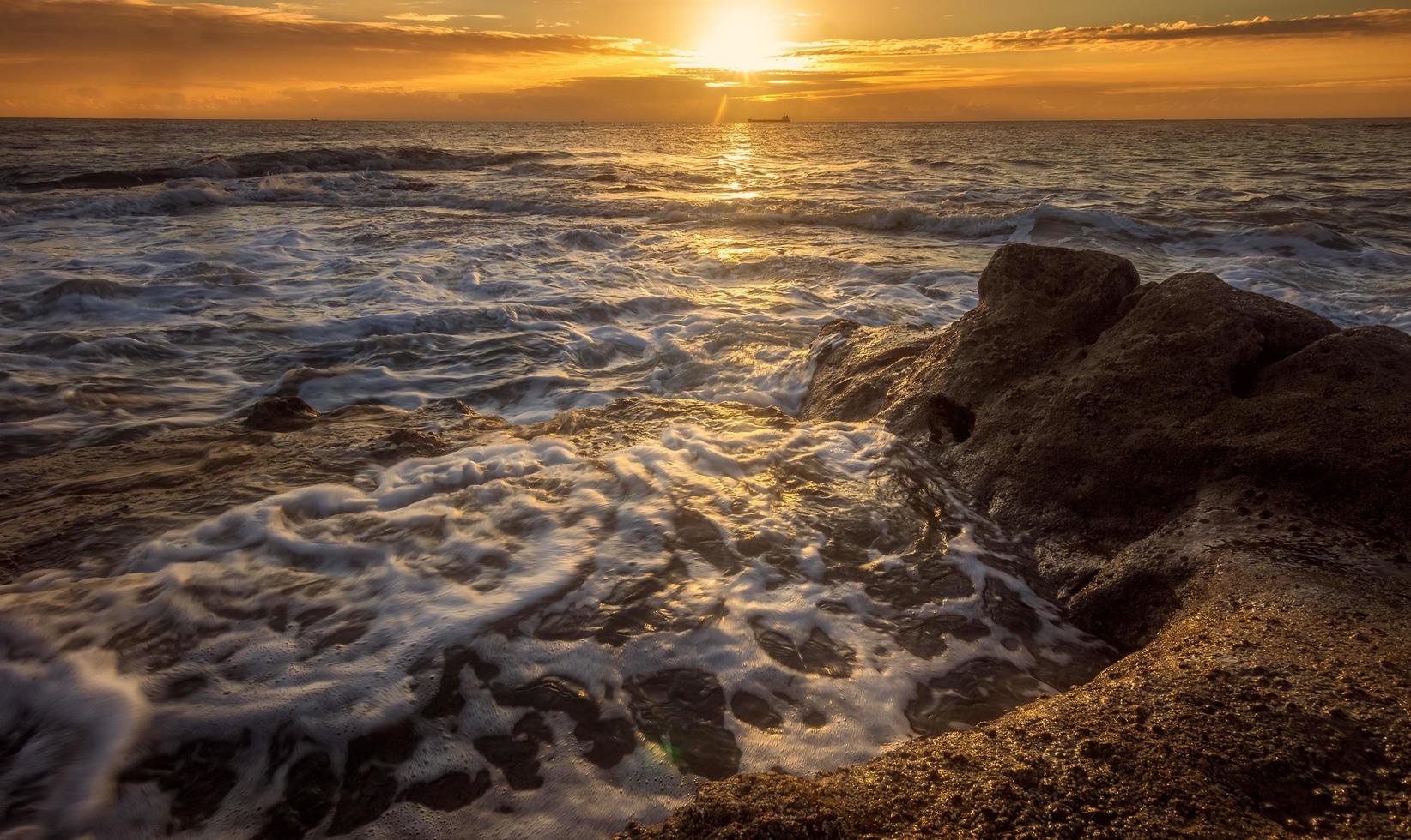 Ocean waves crashing on shore during sunset photo