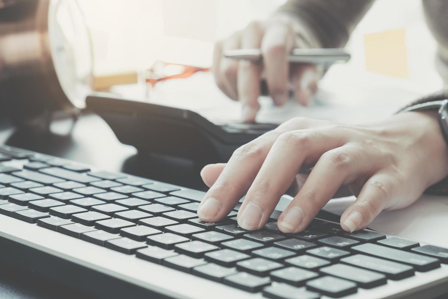 profesional de negocios escribiendo en el teclado mientras usa la calculadora foto